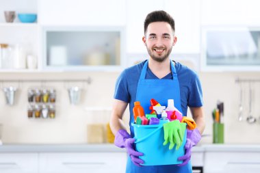 Plastik kova fırçalar, eldiven ve deterjanlar ile mutfakta tutan adam