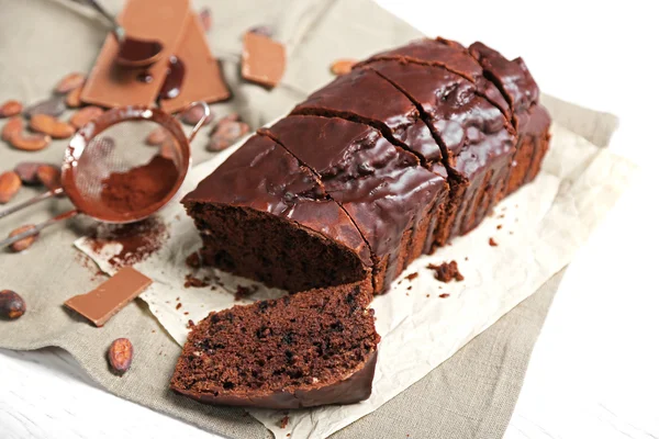 Chocolate sliced cake with icing and cocoa powder on tablecloth — Stock Photo, Image