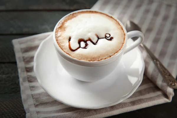 Tasse heißen Cappuccino mit Schokoladensirup und Löffel auf einem schwarzen Holztisch — Stockfoto