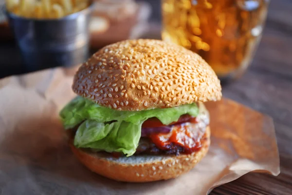 Großer leckerer Hamburger auf Papier mit hellem Bier im Glasbecher, Nahaufnahme — Stockfoto