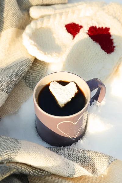 Tazza di caffè caldo con marshmallow cuore e vestiti caldi su sfondo innevato, primo piano — Foto Stock