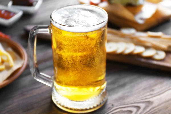 Caneca de vidro de cerveja leve com lanches na mesa de madeira escura, close-up — Fotografia de Stock