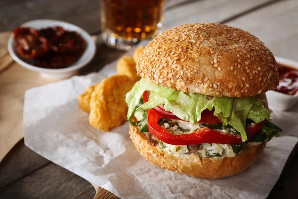 Großer leckerer Hamburger mit Snacks und Glas Bier auf Holztisch — Stockfoto