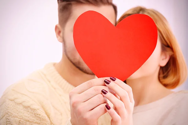 Casal segurando coração vermelho perto de rostos — Fotografia de Stock