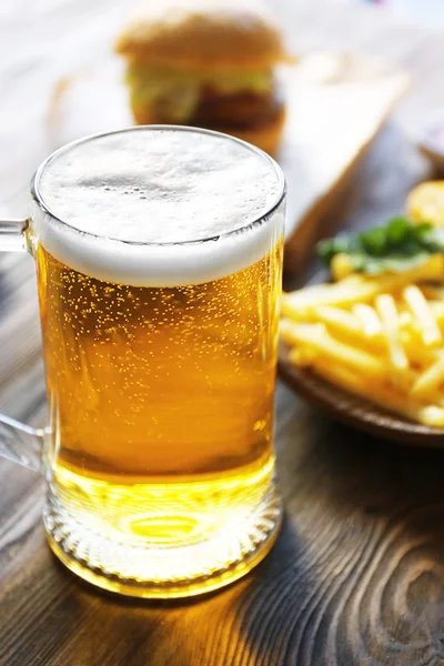 Glazen mok light bier met frietjes op donkere houten tafel, close-up — Stockfoto