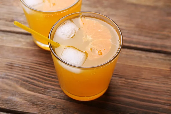 Vasos de zumo de naranja con bloques de hielo y túbulo sobre fondo de madera —  Fotos de Stock