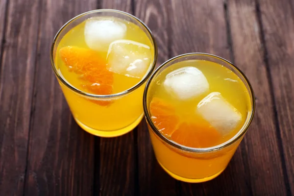 Vasos de zumo de naranja con bloques de hielo y rebanada de fruta sobre fondo de madera — Foto de Stock