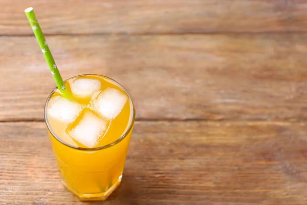 Vaso de zumo de naranja con bloques de hielo y túbulo sobre fondo de madera — Foto de Stock