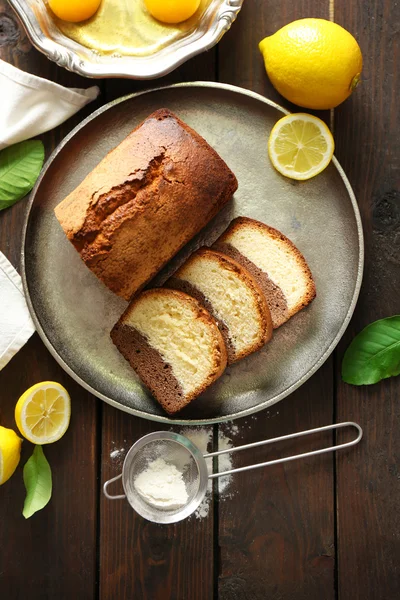 Delicioso pan de pastel dulce en bandeja de metal con limones en la mesa de madera, vista superior —  Fotos de Stock