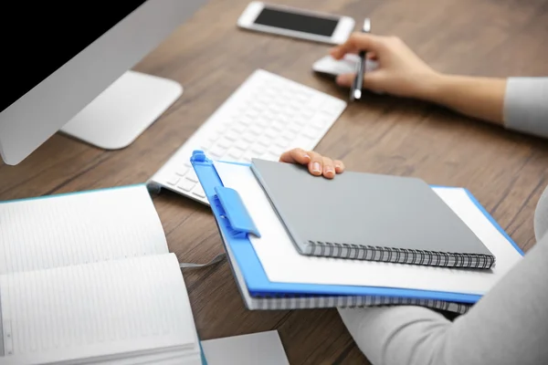 Conceito de trabalho. Clipboard e caderno em mãos de mulher. Computador e telefone inteligente na mesa de madeira — Fotografia de Stock