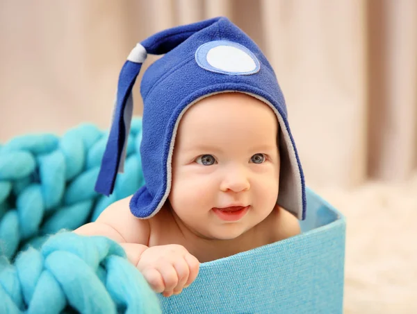 Αξιολάτρευτο μωρό με το αστείο καπέλο κάθεται σε κουτί με τιρκουάζ Πλεκτό ριχτάρι, κοντινό πλάνο — Φωτογραφία Αρχείου