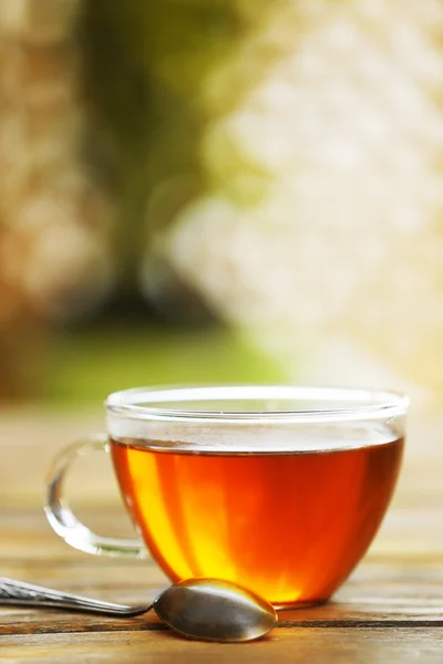 Glass cup of tea on wooden table against blurred background — Stock Photo, Image