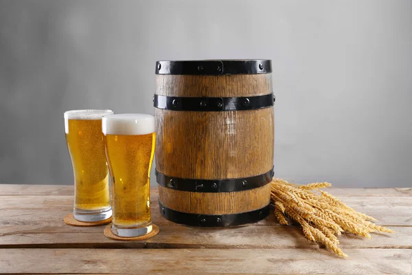 Biervat en glazen bier met tarwe op houten tafel tegen de grijze achtergrond — Stockfoto