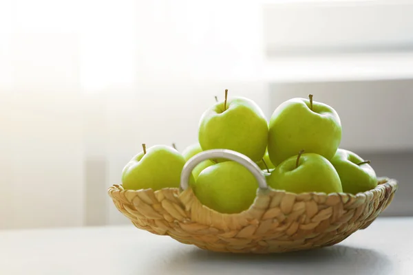 Reife grüne Äpfel in einem Weidenkorb auf einem Küchentisch — Stockfoto