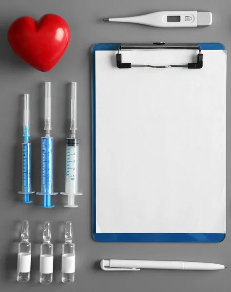 Mesa médica com injeções, termômetro, prancheta, caneta e coração vermelho, vista superior — Fotografia de Stock