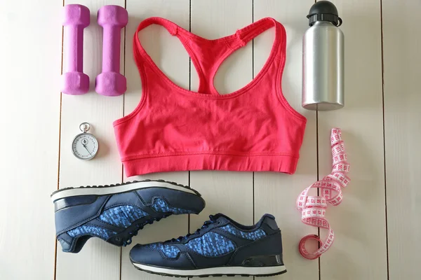 Conjunto de atletas com roupas femininas, equipamentos e garrafa de água sobre fundo branco de madeira — Fotografia de Stock