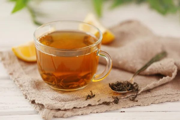 Glass cup of green tea with sliced lemon on wooden table with sackcloth closeup — Stock Photo, Image