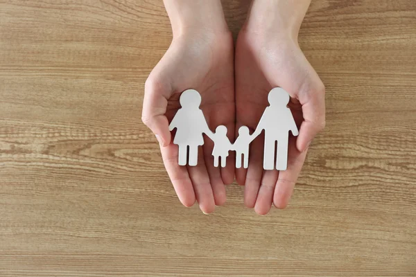 Mani femminili che tengono figura di famiglia su sfondo di legno — Foto Stock