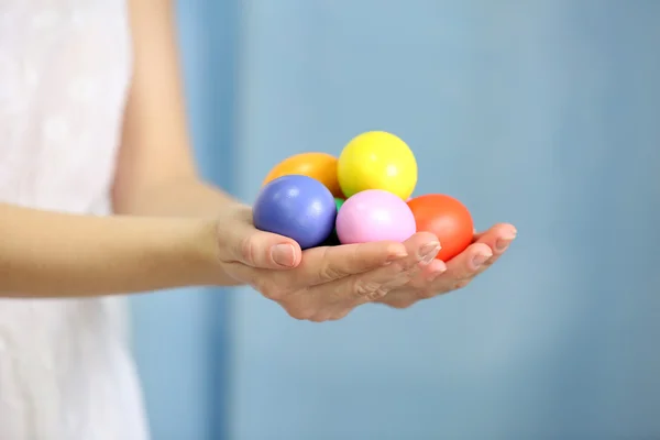 Manos femeninas sosteniendo huevos de Pascua sobre un fondo de cortina azul — Foto de Stock