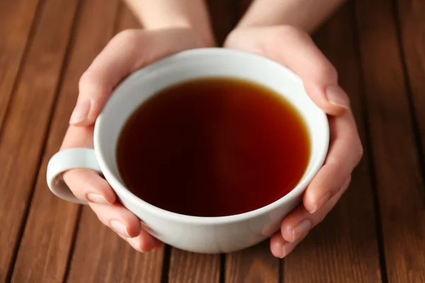 Manos femeninas sosteniendo taza de té sobre fondo de madera —  Fotos de Stock