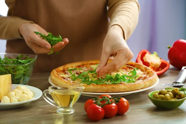 Frau dekoriert frisch gebackene Pizza mit Rucola, Nahaufnahme — Stockfoto