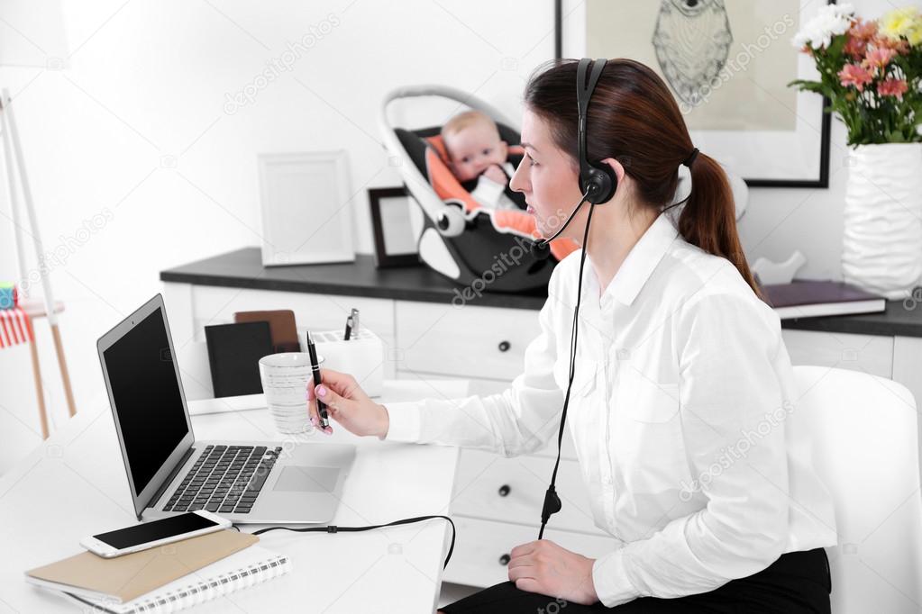 Businesswoman with baby boy working from home using laptop and headset