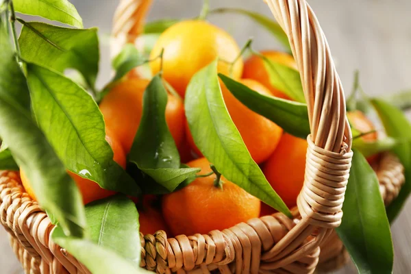 Fresh tangerines with leaves in basket on wooden table, closeup — Stock Photo, Image