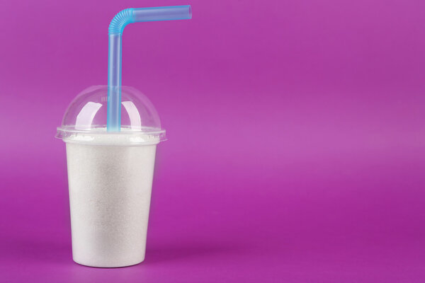 Пластиковая чашка смузи с гранулированным сахаром и коктейльной трубкой на фиолетовом фоне
