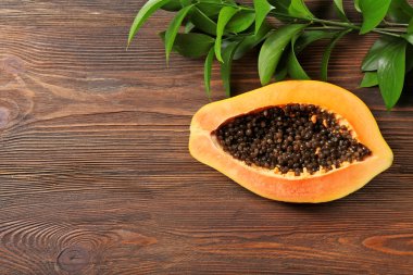 Halved papaya with leaves on wooden background clipart