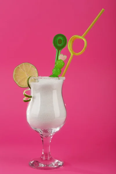 Hurricane glass with granulated sugar, cocktail straw and lime slice on pink background — Stock Photo, Image