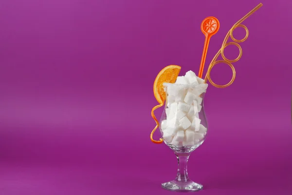 Hurricane glass with lump sugar, cocktail straw and orange slice on purple background
