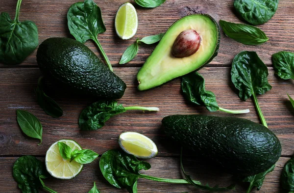 Aguacate en rodajas con espinacas frescas, albahaca y lima sobre fondo de madera, de cerca —  Fotos de Stock