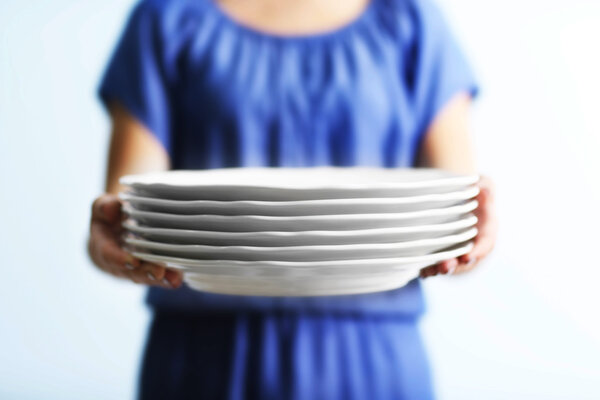 Woman holding plates on light background