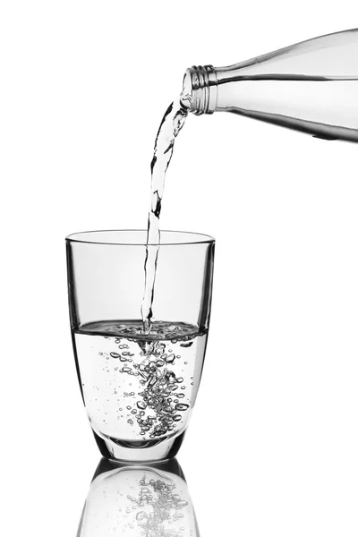 Pouring water from bottle into glass over grey background — Stock Photo, Image