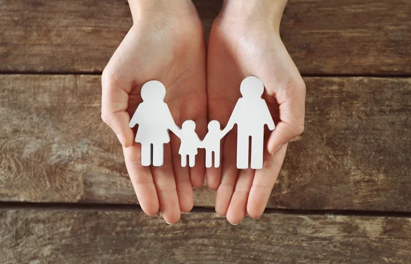 Female hands holding family figure on wooden  background — Stock Photo, Image