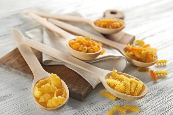 Diferentes tipos de pasta en cucharas sobre fondo de madera —  Fotos de Stock