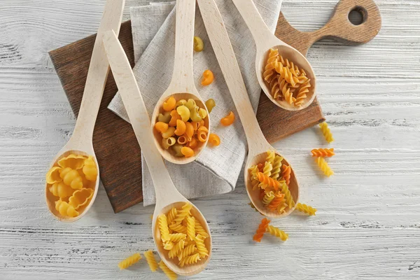 Different types of pasta in spoons on wooden table, top view — Stock Photo, Image