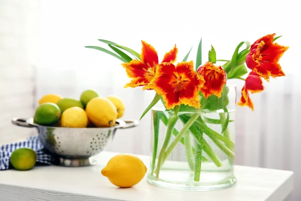 A bouquet of red tulips and bowl of lemons on white table. — Stock Photo, Image