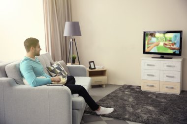 Genç adam evde televizyon izliyor.