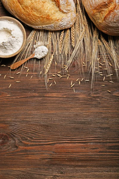 Pane appena sfornato, una ciotola di farina e spighe di grano sullo sfondo di legno — Foto Stock