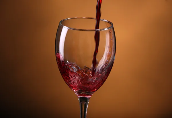 Vino vertiendo en vaso sobre fondo marrón — Foto de Stock