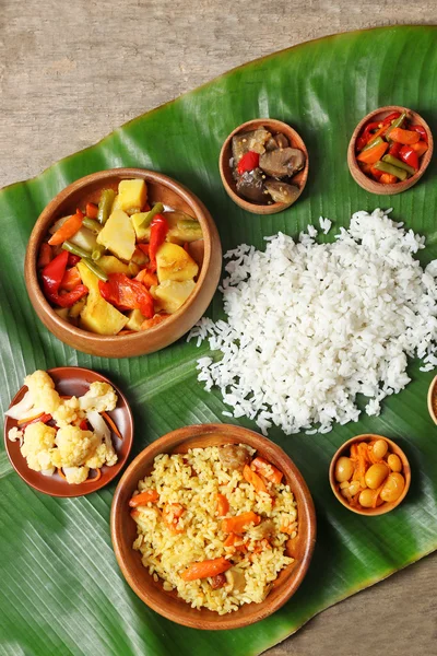 Boiled and fried rice with vegetables on banana leaf over wooden background — Stock Photo, Image