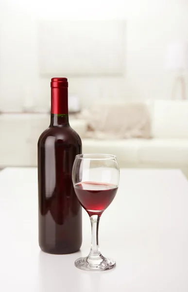 Glas rött vin med flaska på suddig interiör bakgrund — Stockfoto