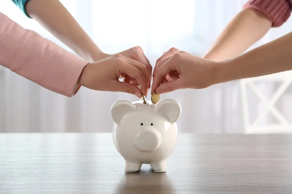 Mãos colocando moeda no banco porquinho — Fotografia de Stock