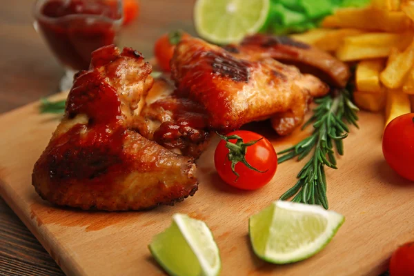 Asas de frango grelhadas com batatas fritas e material de jardim na tábua de corte — Fotografia de Stock