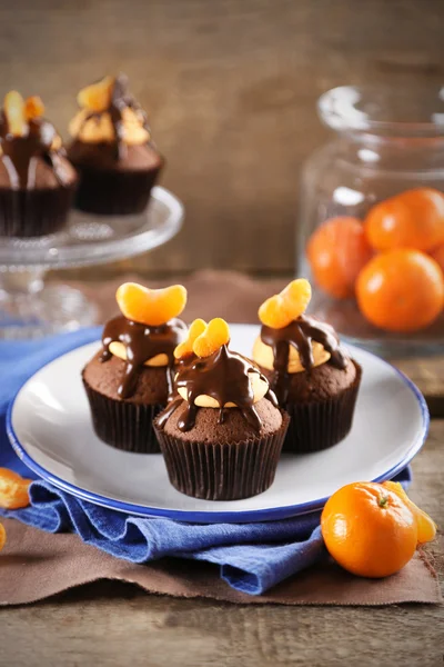 Tre gustosi cupcake con fetta di mandarino e cioccolato su un piatto su fondo di legno — Foto Stock