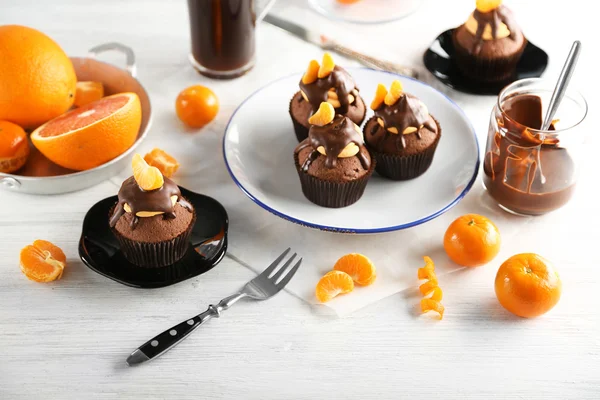 Tasty cupcakes with slice of mandarin and chocolate on a plate over light wooden background — Stock Photo, Image