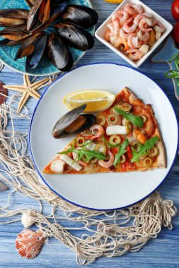 Pizza dilimi deniz ürünleri, kırmızı biber ve mavi ahşap masa üzerinde yeşil zeytin ile