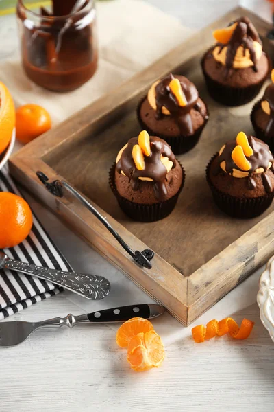 Sabrosos cupcakes con rebanada de mandarina y chocolate en una bandeja sobre fondo de madera clara —  Fotos de Stock