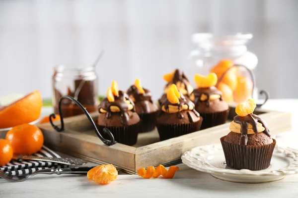 Leckere Cupcakes mit Mandarine und Schokolade auf einem Tablett über hellem Holzgrund — Stockfoto